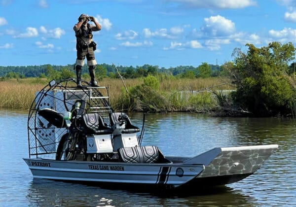 Texas game warden standing on a Patriot law enforcement airboat in the marsh