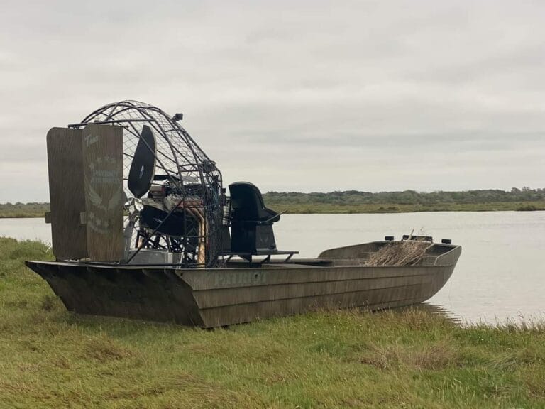 A camo airboat on the grass at the water's edge