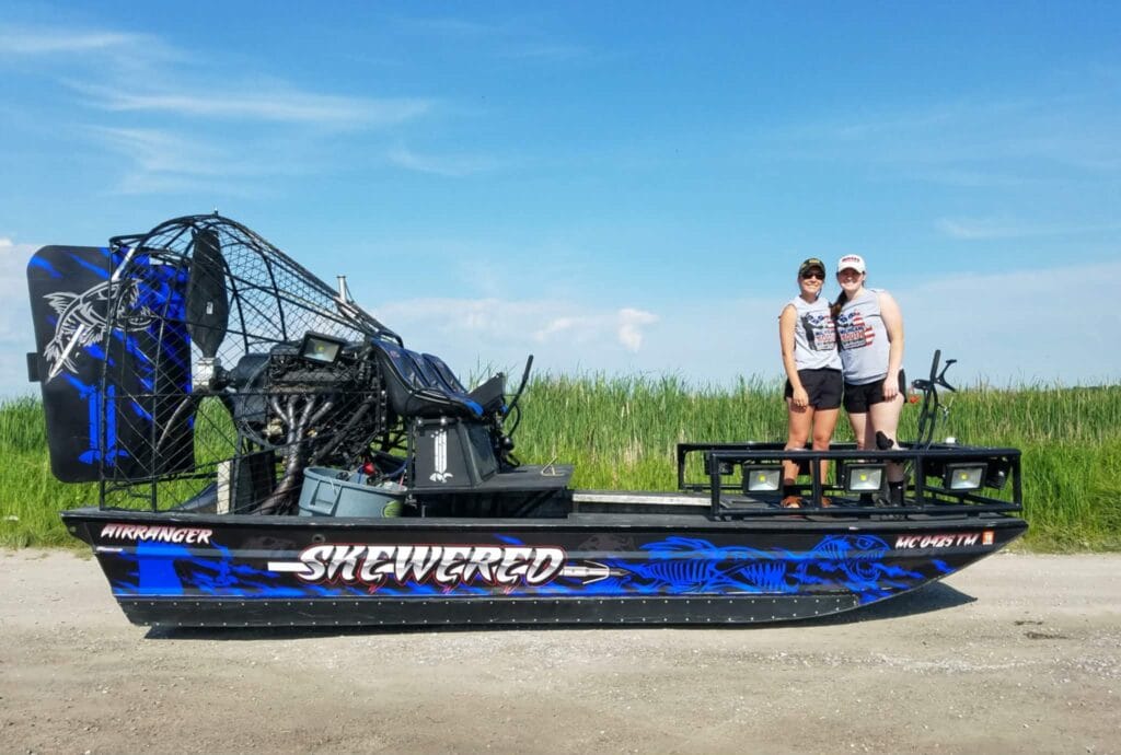 A blue Skewered bowfishing airboat and its owners on the bank