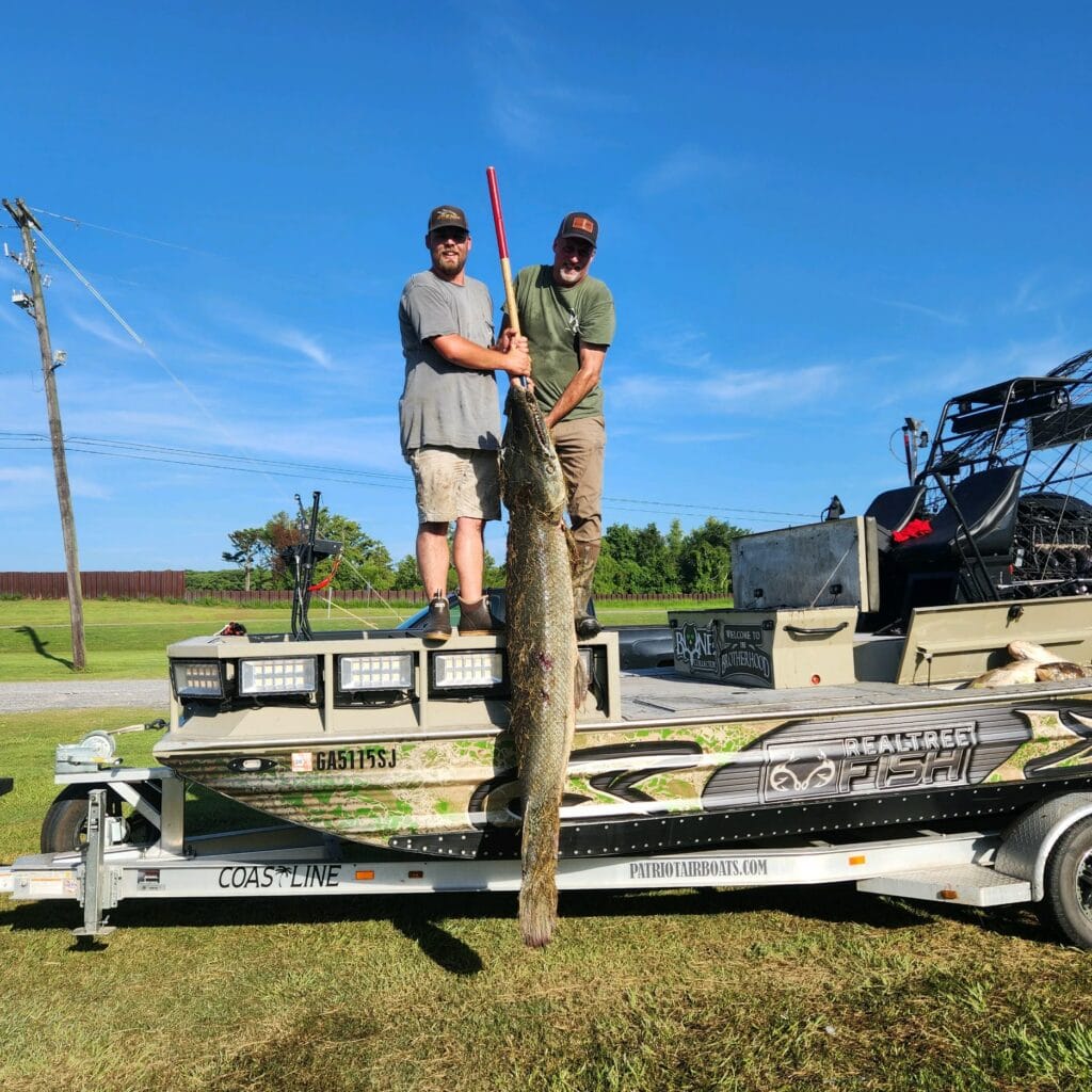 Two anglers holding up a gar beside their Patriot airboat
