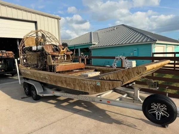 2019 AirRanger 20x8 airboat in grass camo wrap on a tandem trailer beside a shop
