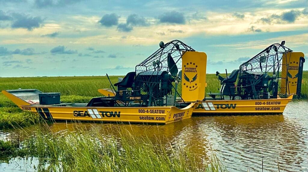 Two matching yellow Sea Tow Patriot airboats side by side in marsh grass