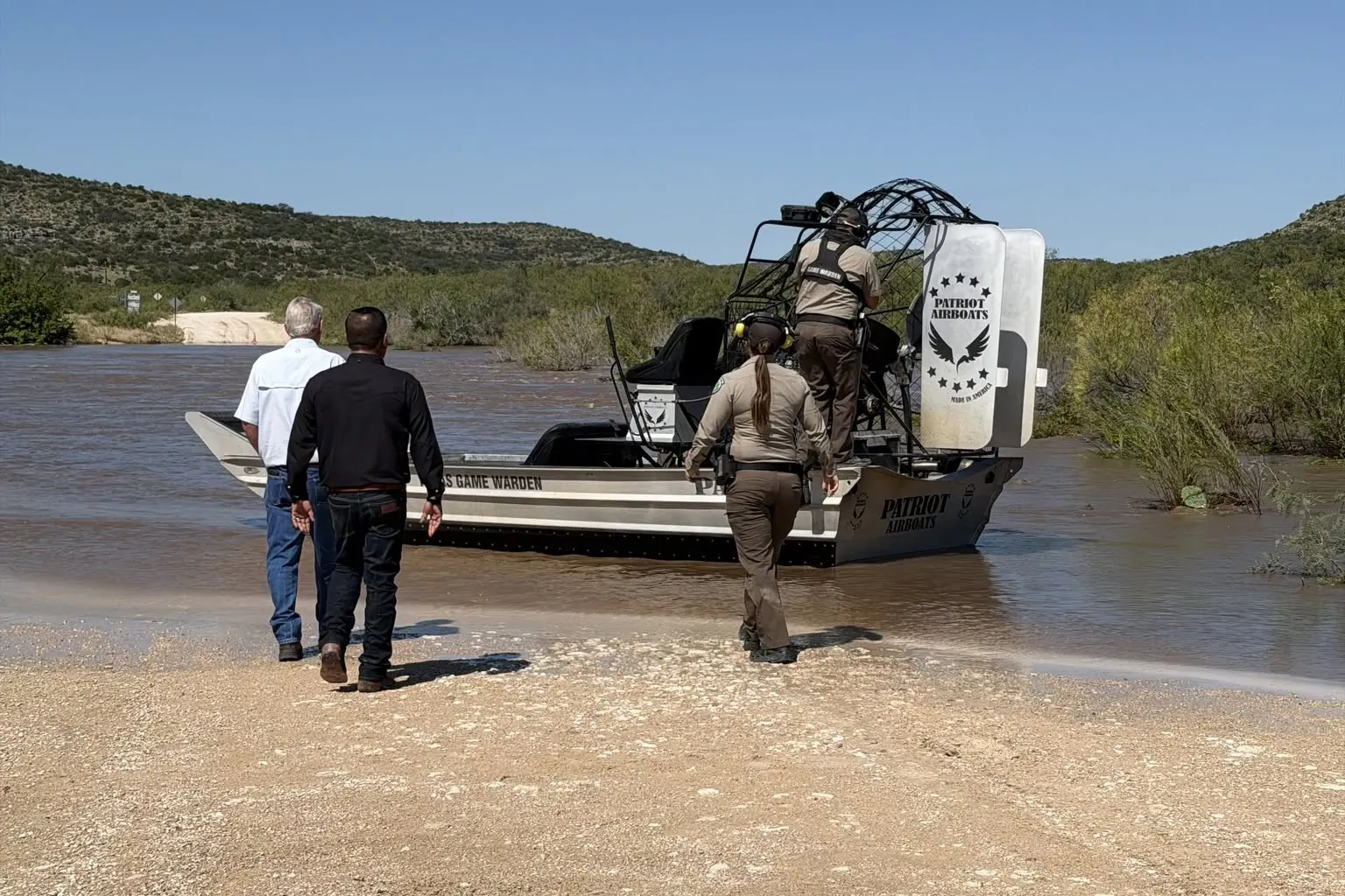Texas Game Wardens boarding a Patriot airboat marked Texas Game Warden at a flooded Dolan Creek Road crossing in Val Verde County, Texas