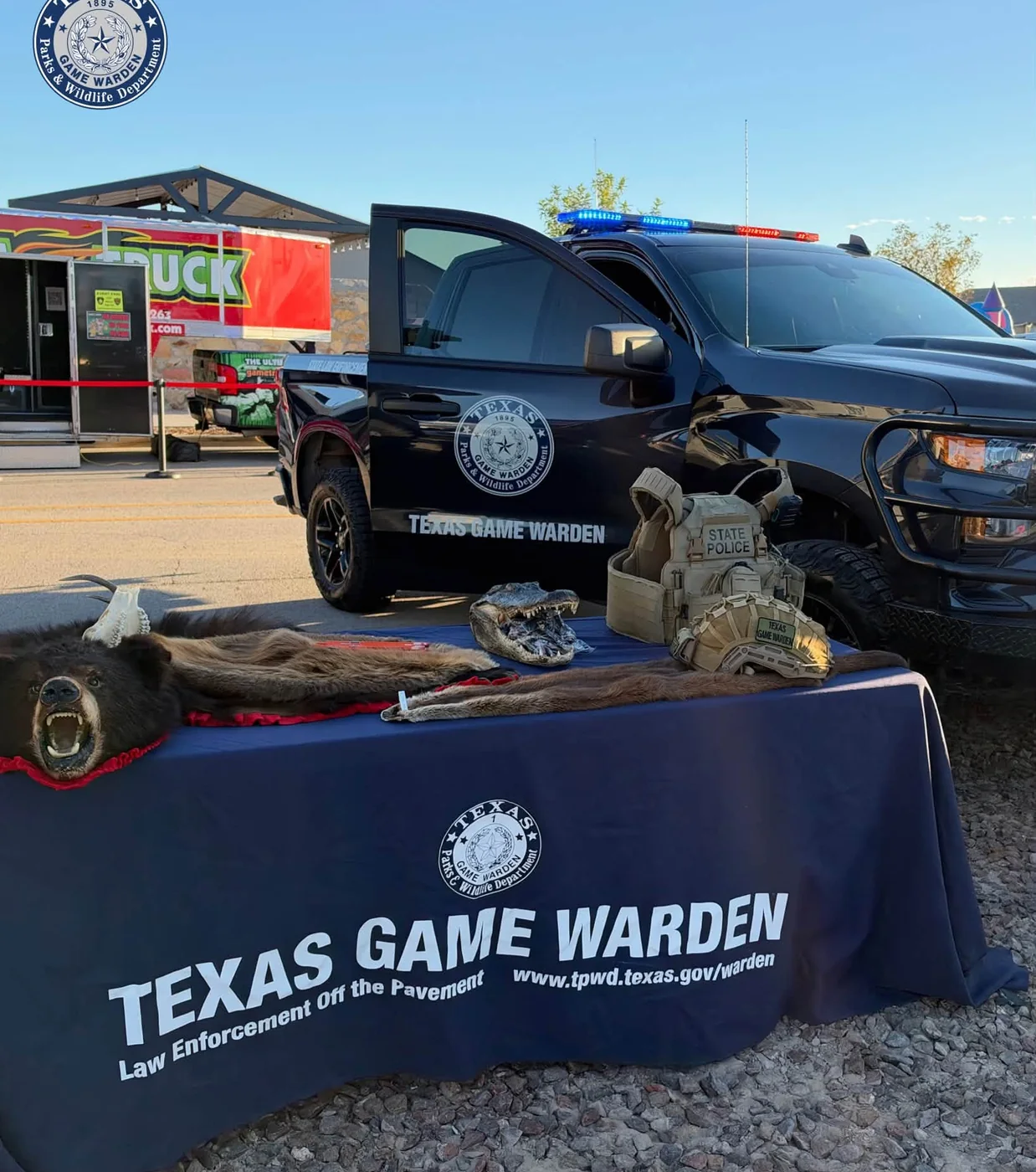 Texas Game Warden display table with hides, an alligator skull and a patrol vest in front of a marked truck