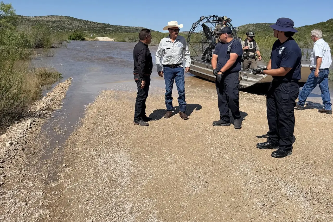 County officials and fire rescue crew talking on the gravel bank with a Patriot airboat idling in the floodwater behind them